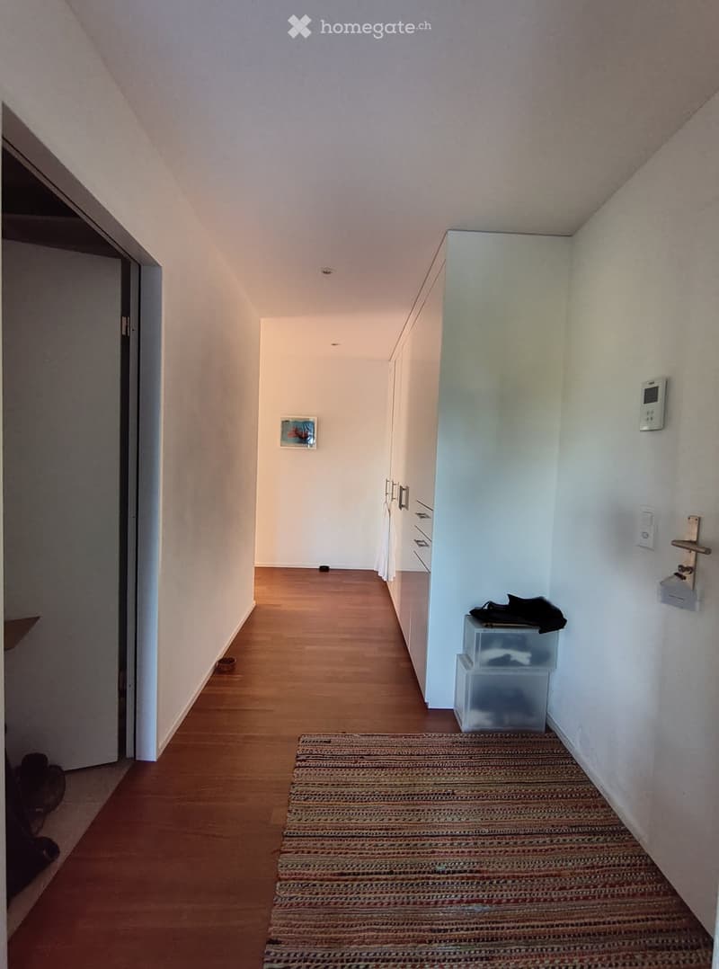 A narrow hallway with wooden flooring, white walls, and a small rug placed on the floor. There are storage bins and a small picture frame visible on the walls.