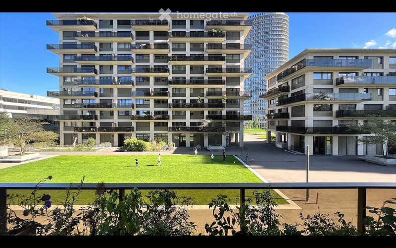 Modern multi-story residential building with balconies and a spacious green courtyard area.
