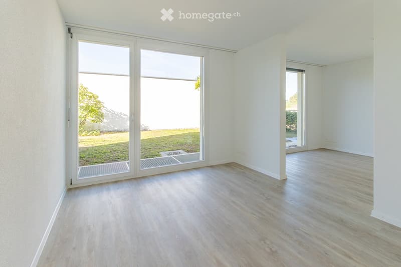 Empty room with light wooden flooring, white walls, and large sliding glass doors leading to a grassy outdoor area.