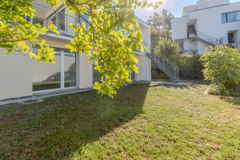 Modern house with a well-maintained lawn, glass balcony, and staircase leading to an upper level.