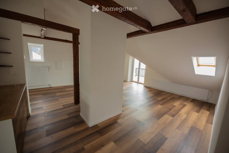 Empty attic space with wooden beams, wooden flooring, and natural light from skylights and windows. No furniture or furnishings present.