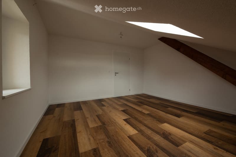 Empty attic room with wooden flooring, white walls, and a skylight window. No furniture or equipment present.