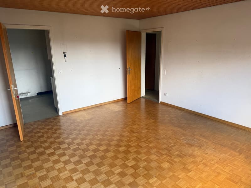 Empty room with wooden flooring, light-colored walls, and two open doors leading to other spaces.