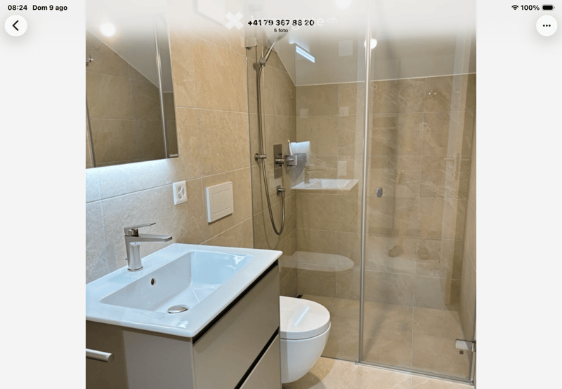 Modern bathroom with beige tiles, a white sink with a chrome faucet, a large mirror, a toilet, and a glass-enclosed shower stall.