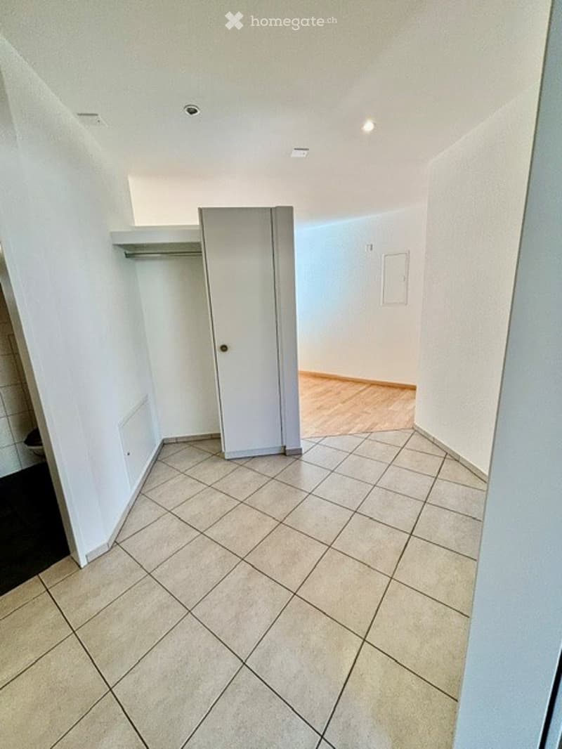 Empty hallway with tiled floor and white walls, featuring a closed closet door and a small shelf on the left side.