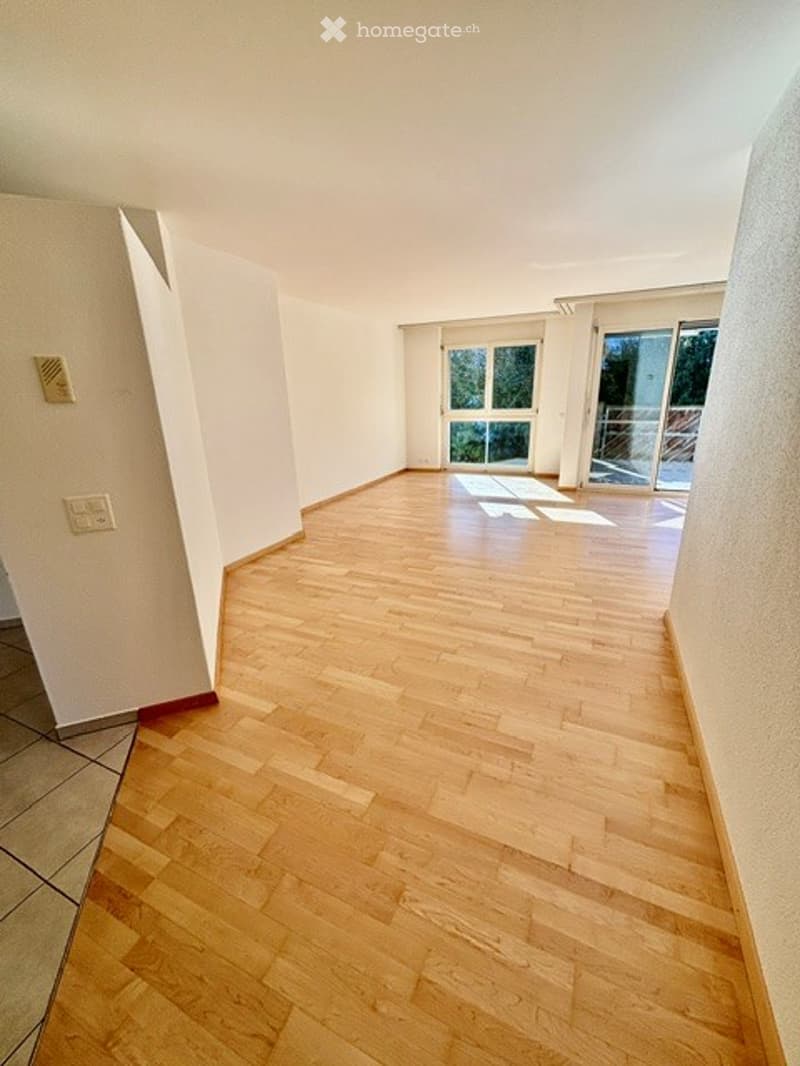 Empty room with light wooden flooring, white walls, and large glass doors leading to a balcony.