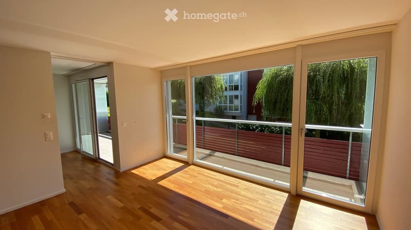 Empty room with wooden flooring, large sliding glass doors leading to a balcony, and white walls.