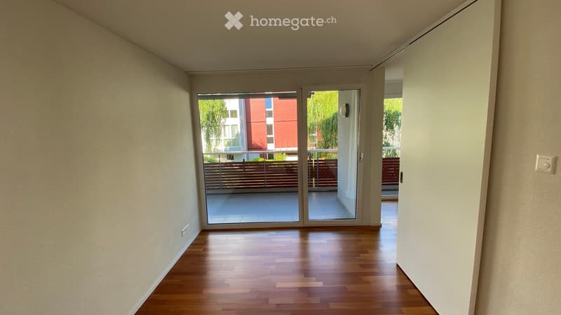 Empty room with wooden flooring, white walls, and a large sliding glass door leading to a balcony.