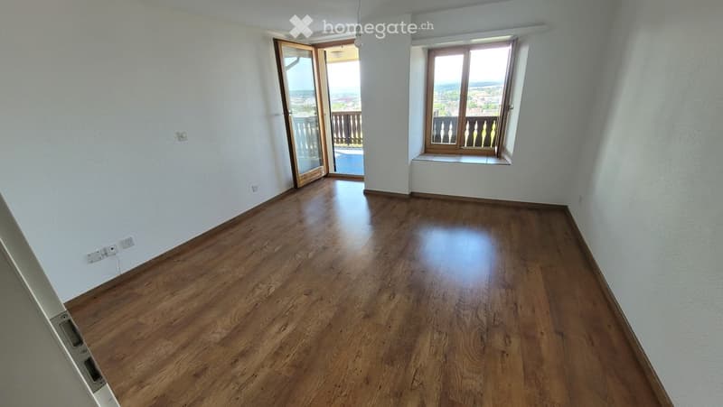 Empty room with wooden flooring, white walls, large window, and sliding glass door leading to a balcony.