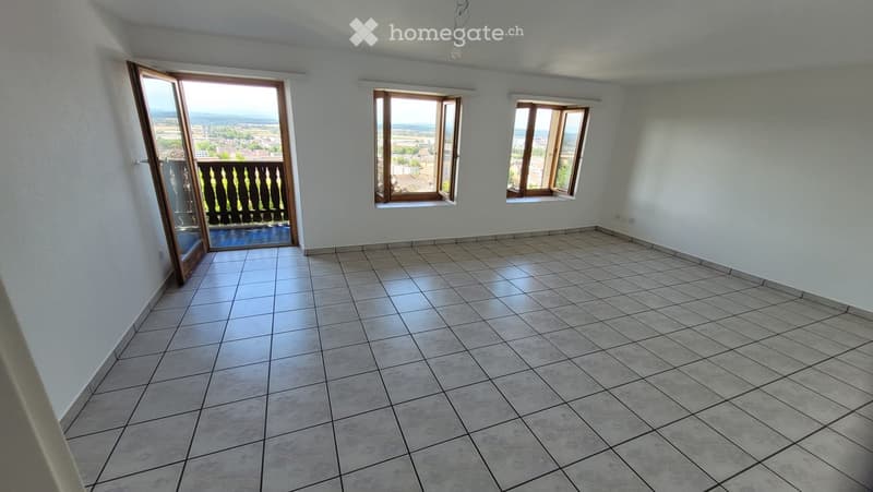 Empty room with tiled floor, white walls, and large windows offering a scenic view. Features an open sliding door leading to a balcony.