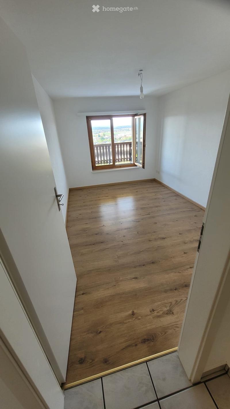 Empty room with wooden flooring, white walls, and a window opening to a balcony.