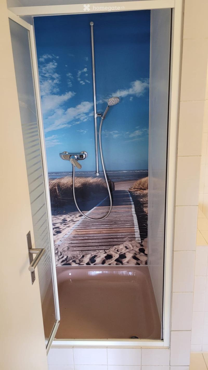Bathtub with a beach-themed mural on the wall, featuring a showerhead and faucet.