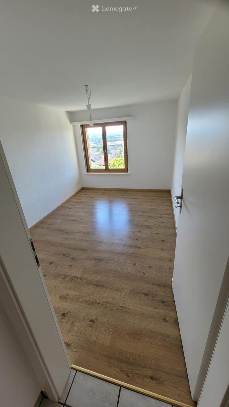 Empty room with wooden flooring, white walls, and a window with wooden frame showing a view of the outside.