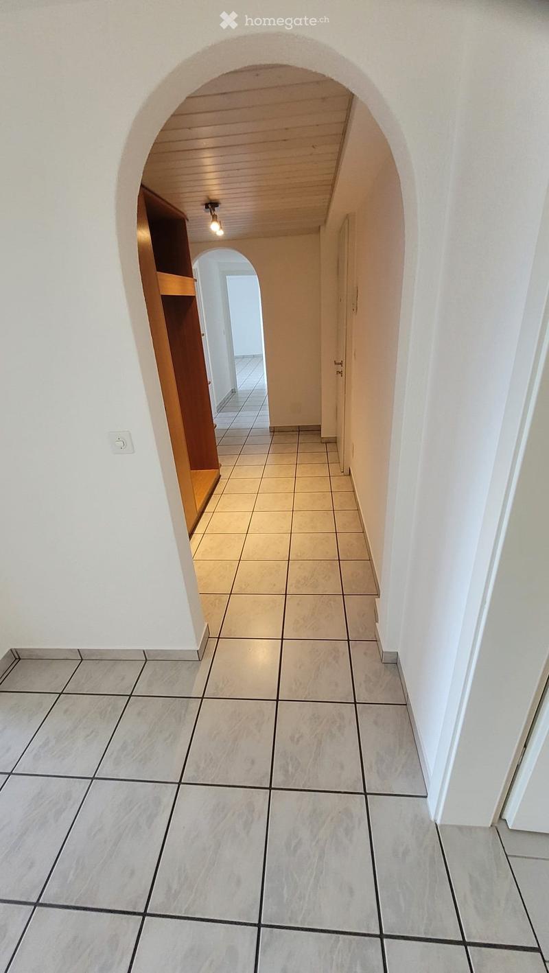 A clean, well-lit hallway with tiled floors and white walls, featuring an arched doorway leading to another room.