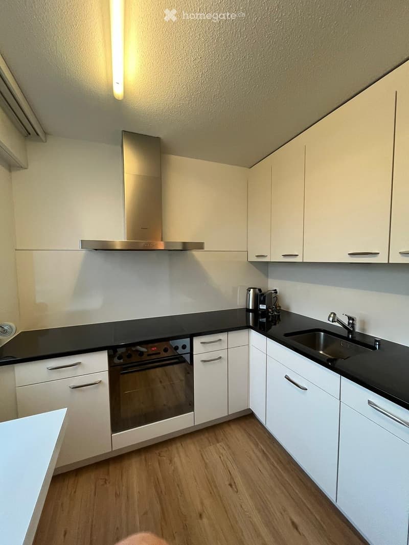 Modern kitchen with white cabinets, black countertops, stainless steel oven, sink, and coffee maker.