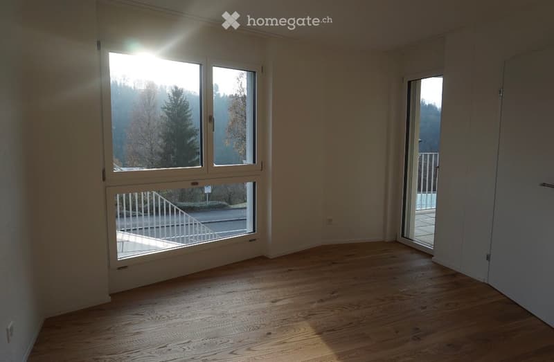 Empty room with wooden flooring, large windows, and a sliding glass door leading to a balcony.