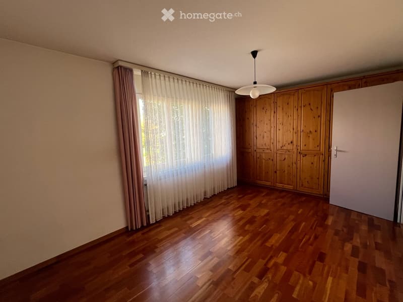 Empty room with wooden flooring, large window with curtains, and built-in wooden closet.