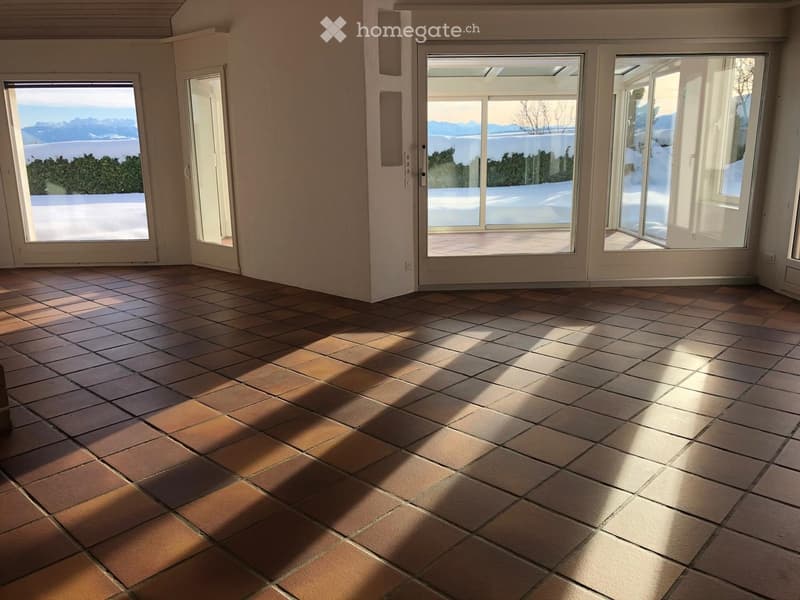 Empty room with tiled floor and large windows offering a scenic view of the ocean and mountains.