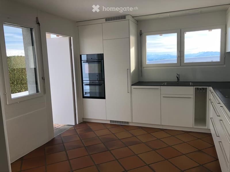Modern kitchen with white cabinets, tiled floor, large windows offering a scenic view, and built-in oven.