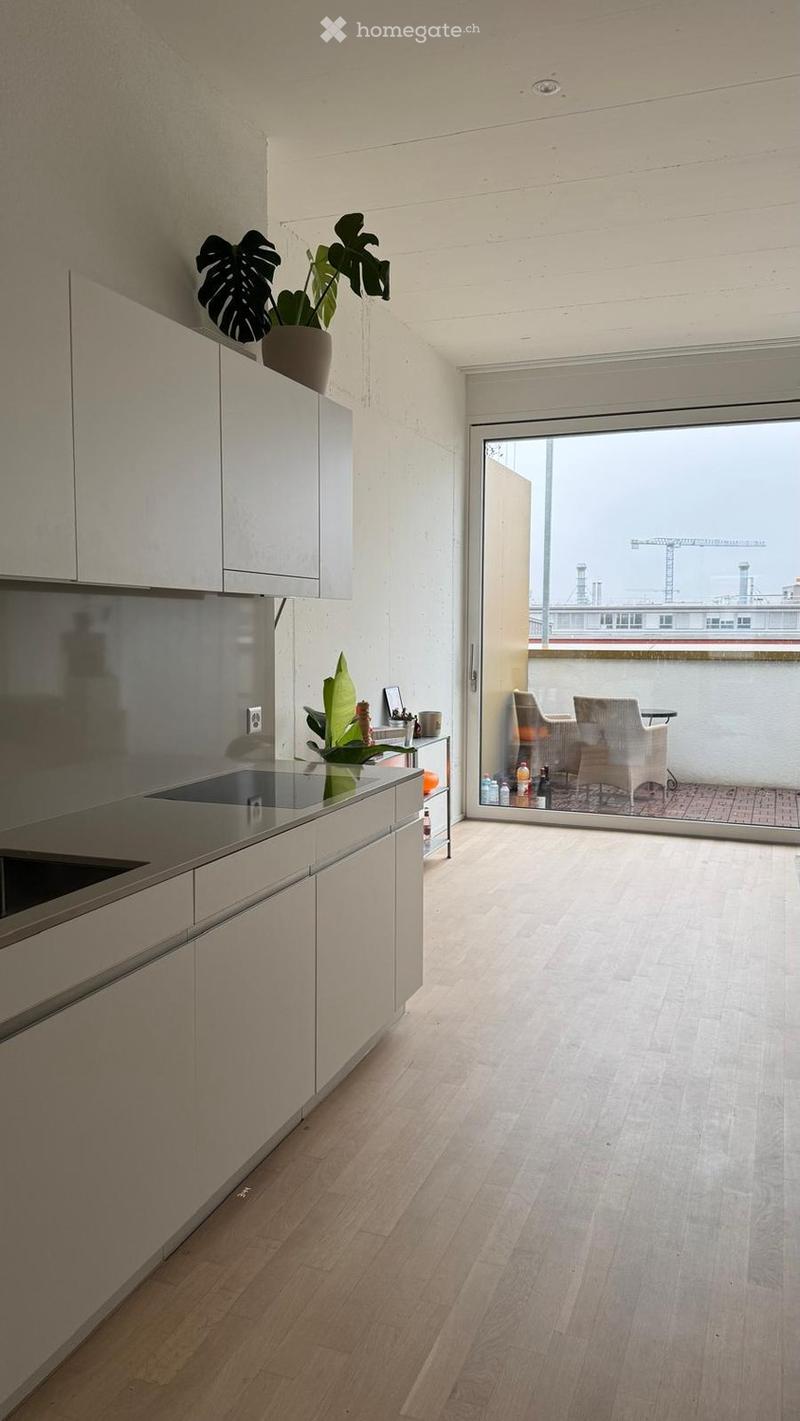 Modern kitchen with light-colored cabinets, an induction cooktop, and a small table with chairs on a balcony.
