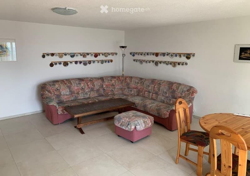 Living room with a patterned sofa, wooden coffee table, ottoman, and wooden chairs around a small table. The walls are decorated with a collection of circular items arranged in rows.
