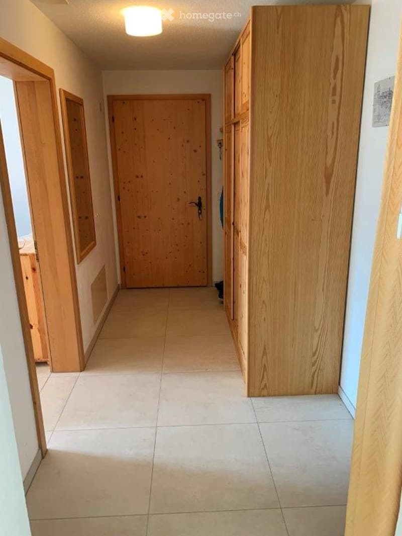 A clean, well-lit hallway with tiled flooring, wooden doors, and built-in wooden cabinets on one side.