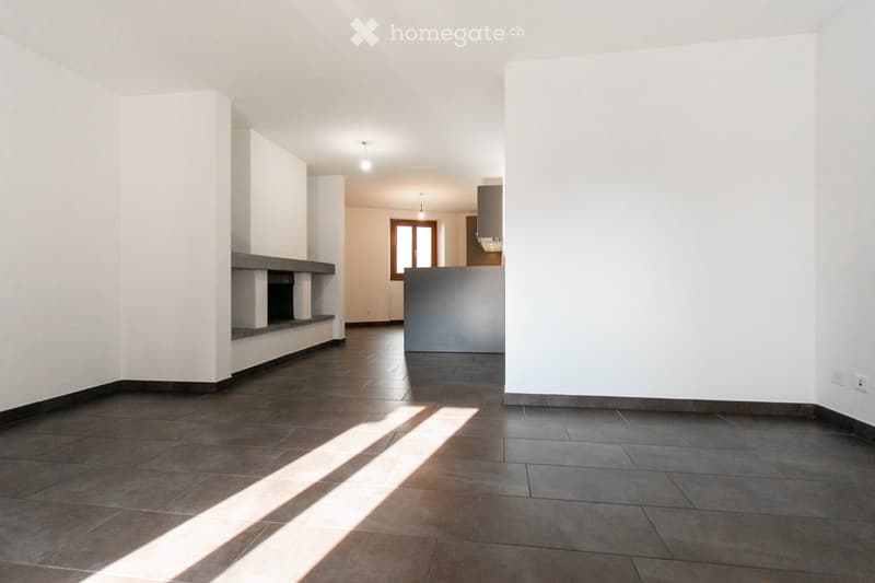 Empty room with dark tiled floor, white walls, and a built-in fireplace. Natural light streams in from a window in the background.