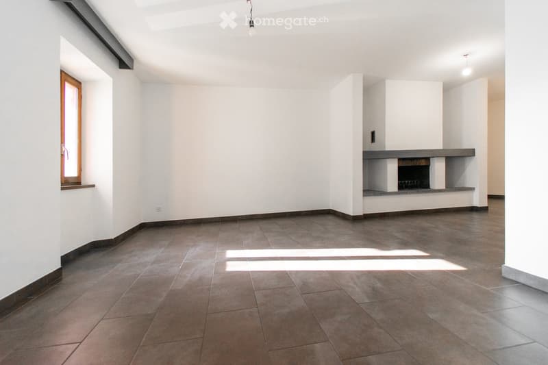 Empty room with tiled floor, white walls, and a built-in fireplace. Natural light streams in from a window on the left side.