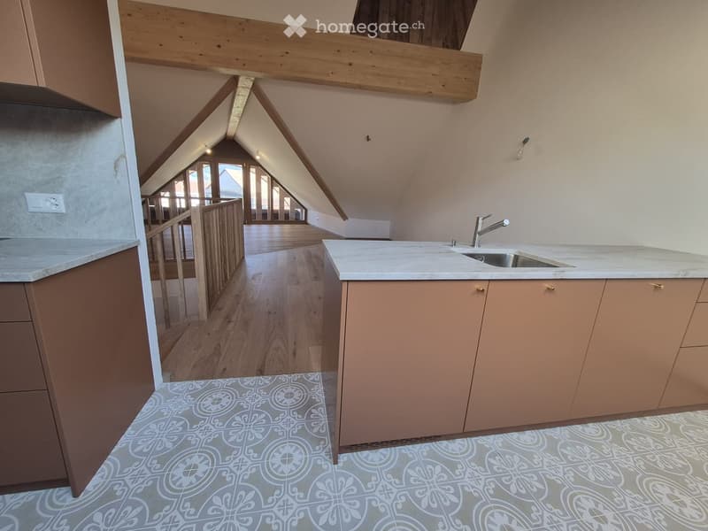 Modern kitchen with light-colored cabinets, marble countertops, and a stainless steel sink. The floor features a decorative tile pattern, and the space includes a wooden staircase leading to an upper level.