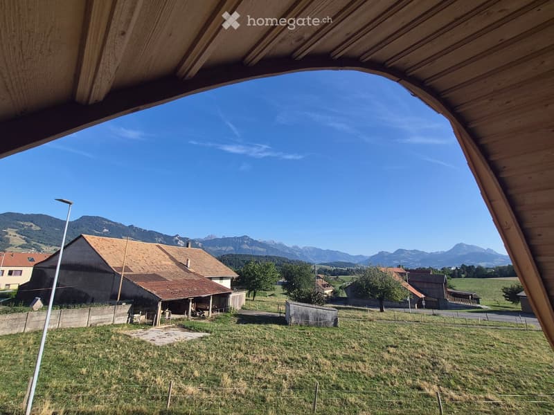 View from a wooden structure showing a rural landscape with houses, a road, and mountains in the background.
