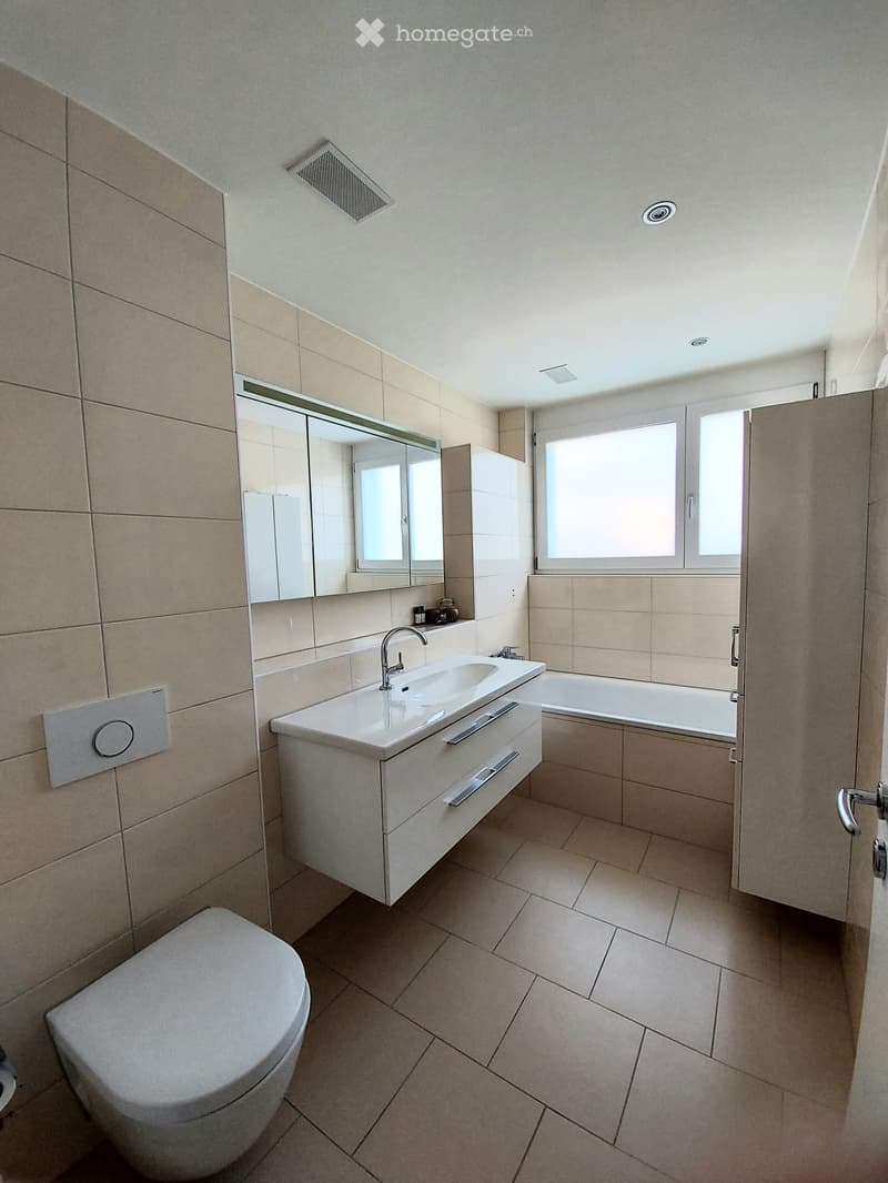 Modern bathroom with beige tiles, a white sink with a chrome faucet, a toilet, a bathtub, and a large mirror above the sink.