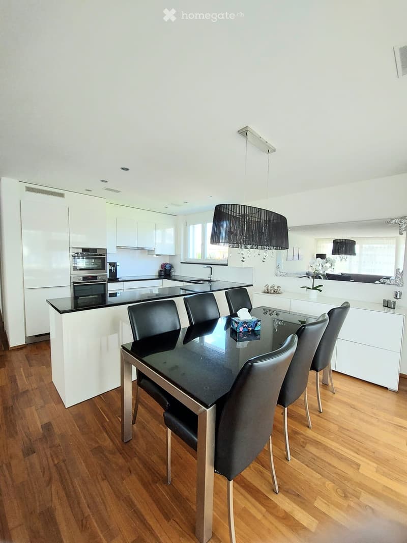 Modern kitchen with white cabinets, black countertops, a dining area with a glass table and black chairs, and a chandelier hanging from the ceiling.