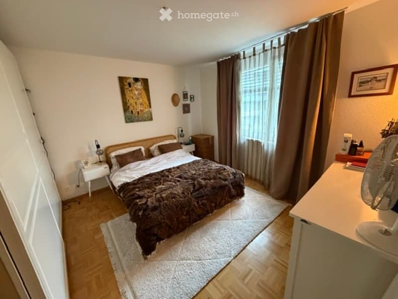 Cozy bedroom with a large bed, nightstand, fan, and artwork on the wall.
