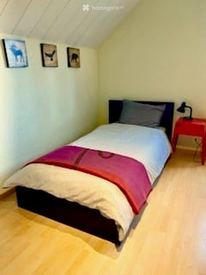 Cozy bedroom with a double bed, red and white bedding, a nightstand with a lamp, and three picture frames on the wall.