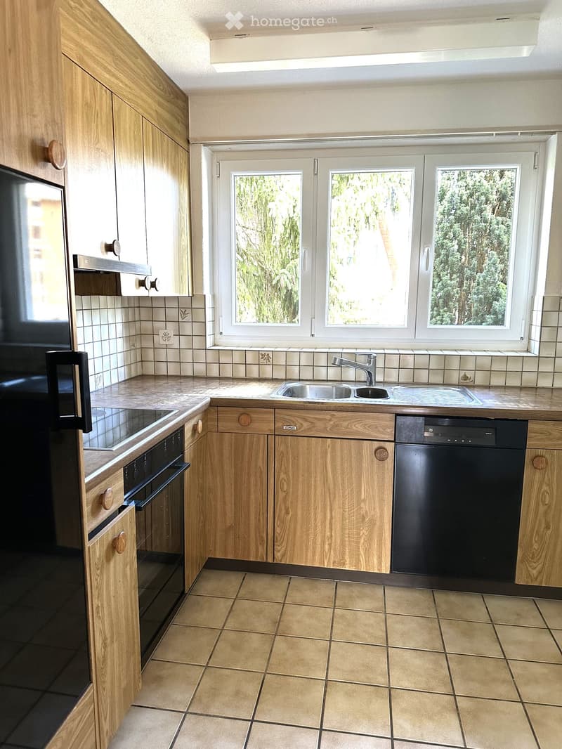 Modern kitchen with light wooden cabinets, tiled backsplash, and stainless steel appliances including an oven, dishwasher, and sink.