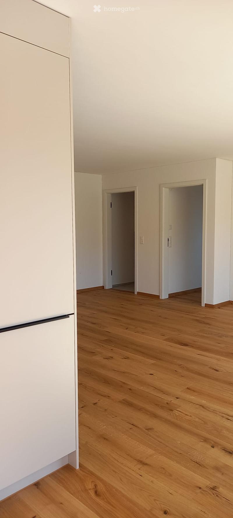 Empty room with light wooden flooring and white walls, featuring two open doorways leading to adjacent spaces.