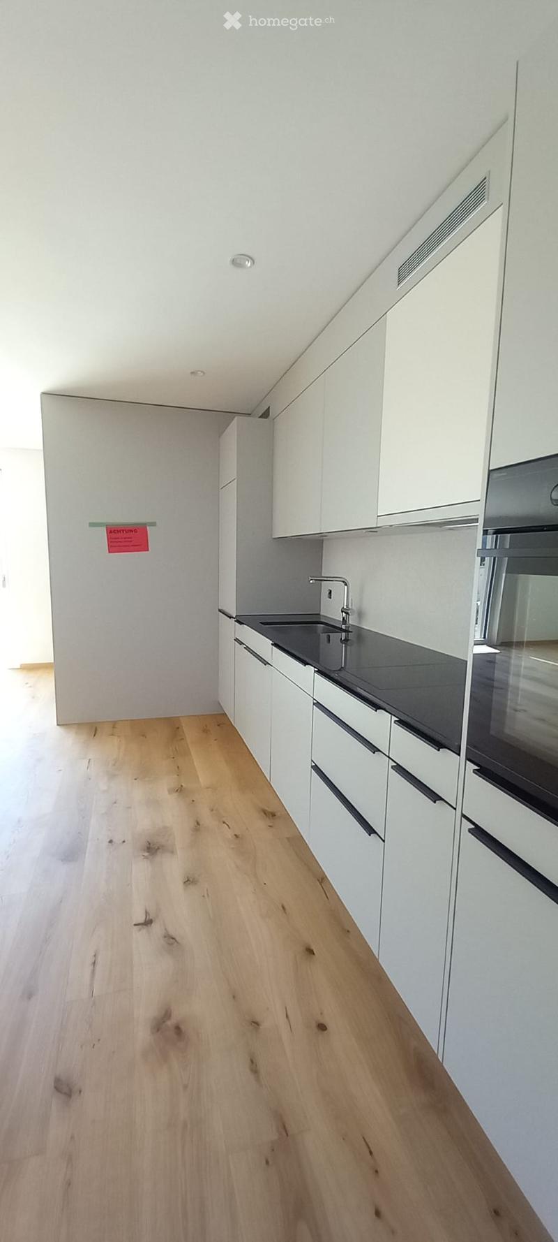 Empty kitchen with white cabinets, black countertop, and wooden flooring. No appliances or furniture present.