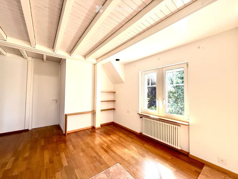 Bright, empty room with wooden flooring, white walls, large windows, built-in shelves, and a radiator under the windows.