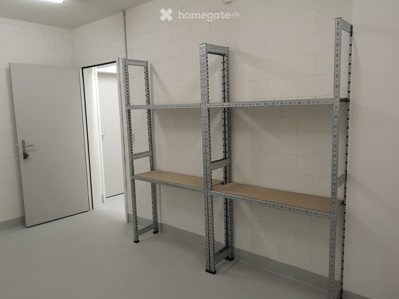 Empty room with white brick walls, grey floor, and metal shelving units with wooden shelves.
