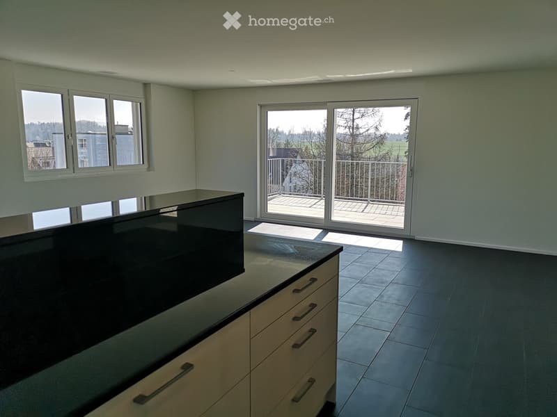 Modern kitchen with dark countertop, light-colored cabinets, and large windows, including a sliding glass door leading to a balcony.