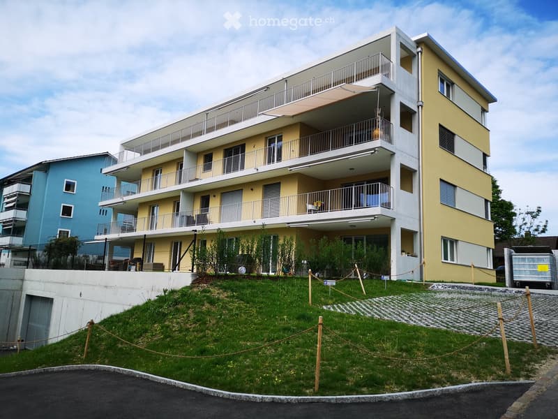 Modern multi-story residential building with balconies, yellow and white facade, and a raised ground floor.