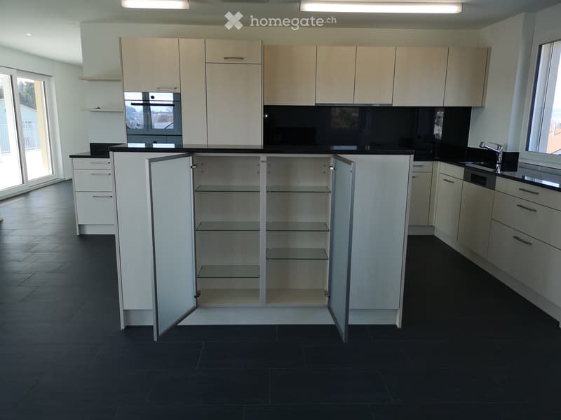 Modern kitchen with white cabinets, black countertops, and dark tiled flooring. Features an island with glass shelves and a sink with a modern faucet.