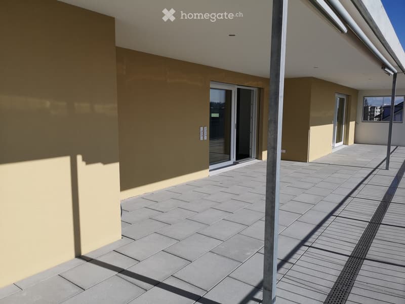 Modern balcony with tiled flooring, glass sliding doors, and a covered section with wooden decking.