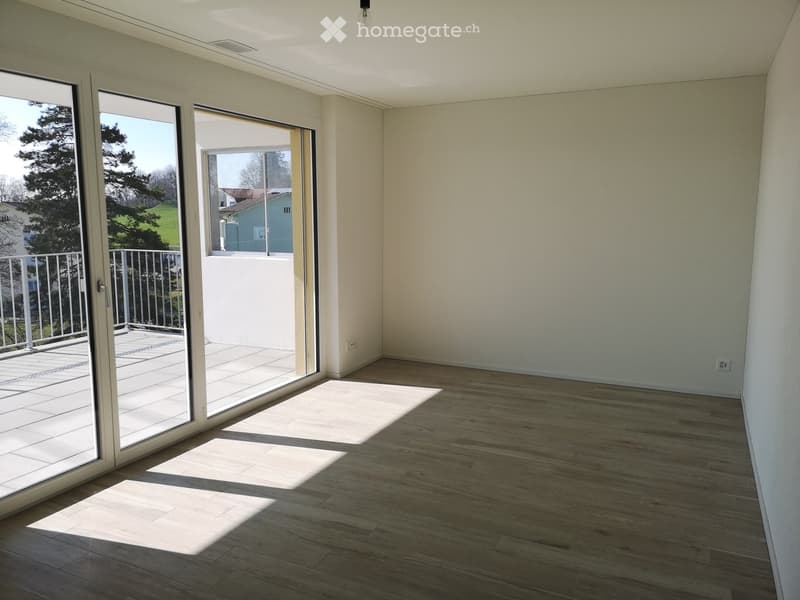 Empty room with wooden flooring, large glass sliding doors leading to a balcony, and natural light streaming in.