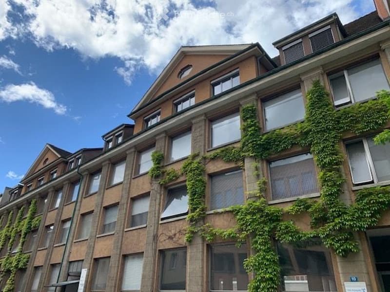 Multi-story brick building with ivy-covered facade, large windows, and a mix of flat and pitched roofs.