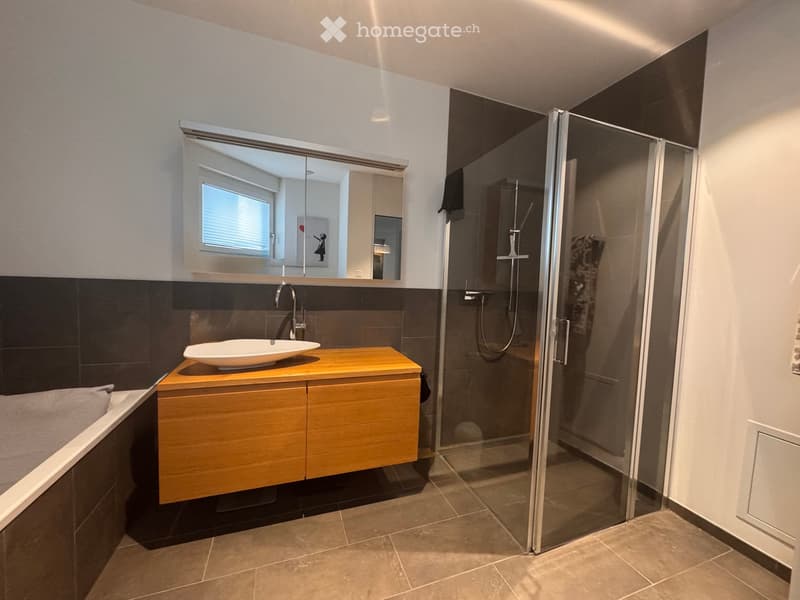Modern bathroom with a wooden vanity, white sink, large mirror, glass-enclosed shower, and bathtub.
