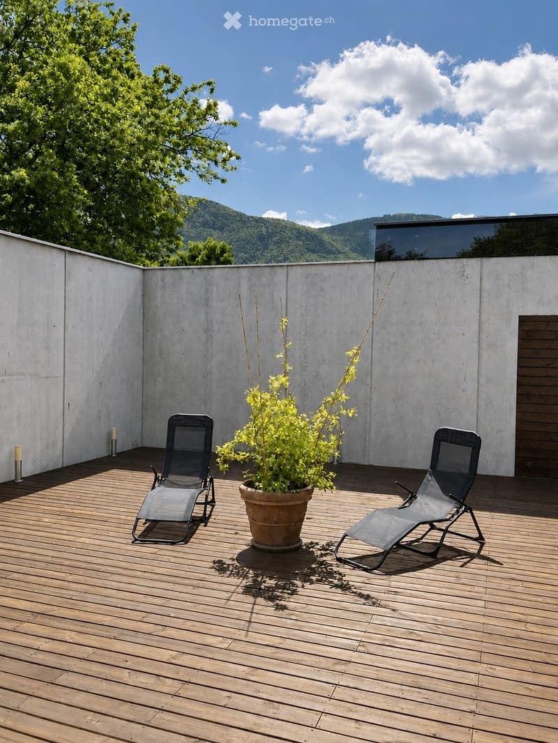 Wooden deck with two lounge chairs and a potted plant, overlooking a scenic mountain view.