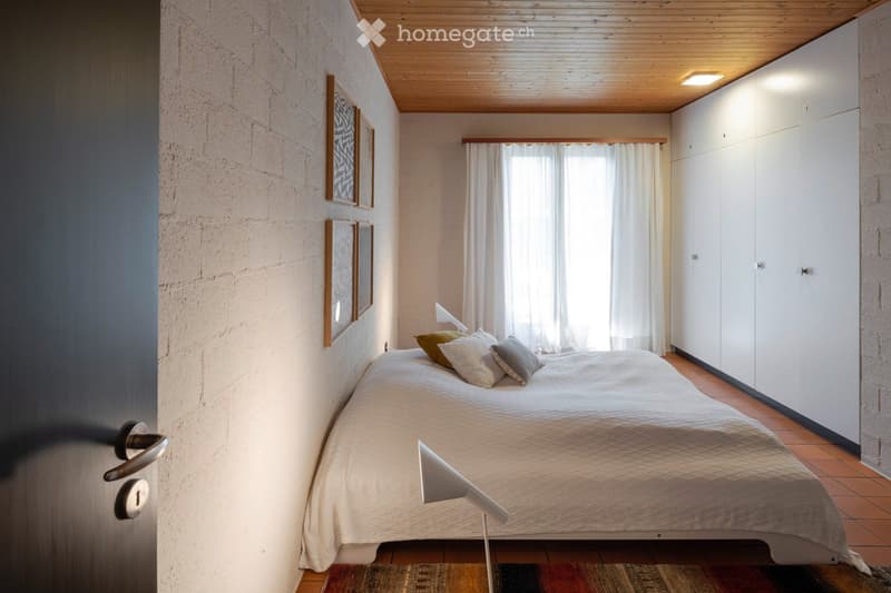 Modern bedroom with a white bed, multiple pillows, a bedside lamp, built-in white wardrobes, and framed artwork on the wall.