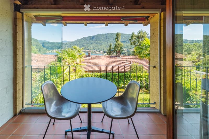 Balcony with a round table and two chairs, overlooking a scenic view of a lake and mountains.