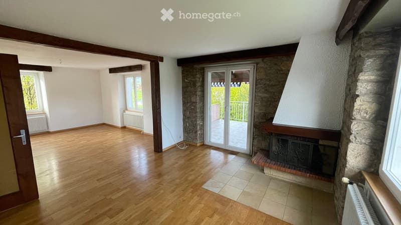 Empty room with wooden flooring, exposed wooden beams, stone fireplace, large windows, and sliding glass door leading to a balcony.